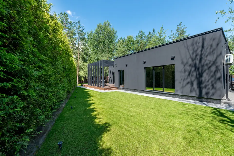 Fresh lawn running the length of a modern charcoal-clad home, framed by a tall privacy hedge